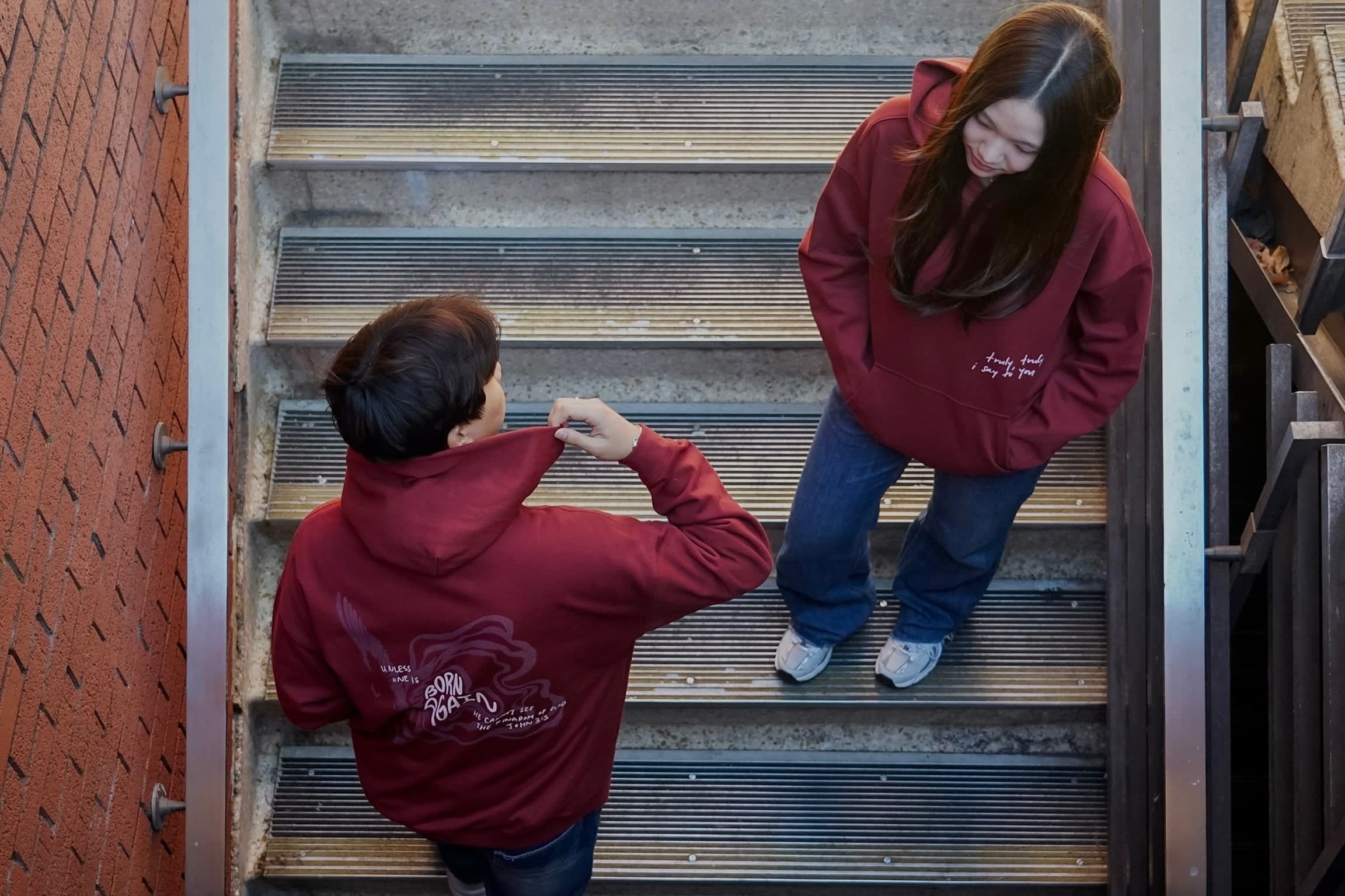 Born Again burgundy hoodies, showing the front and back design on a staircase